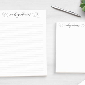 May include: Two white notepad sets with lined paper. The top notepad has the name "audrey stevens" written in cursive script. The bottom notepad has the same name written in cursive script.