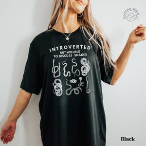 Puede incluir: Camiseta negra con el texto "Introvertido pero dispuesto a hablar de serpientes" y un gr&aacute;fico de varias serpientes.
