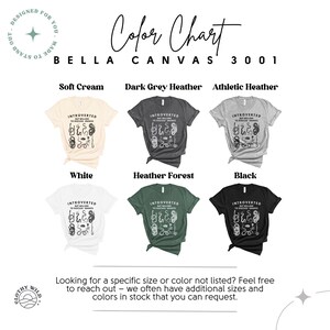 Puede incluir: Carta de colores para camisetas Bella Canvas 3001 en varios colores, incluyendo crema suave, gris oscuro jaspeado, jaspeado atl&eacute;tico, blanco, bosque jaspeado y negro. Cada muestra de color presenta un dise&ntilde;o gr&aacute;fico de una serpiente con el texto "Introvertido pero dispuesto a hablar de serpientes".