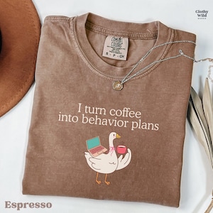 May include: A white ceramic mug with a black handle and the text "But First, Coffee" in a black, handwritten-style font. The mug is on a white surface.