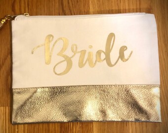May include: A white canvas zippered pouch with a gold zipper and tassel. The pouch has a gold metallic bottom and the word "Bride" written in gold script.