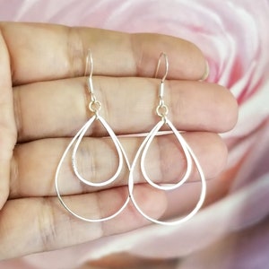 May include: A pair of silver teardrop earrings with a double-layered design. The earrings are made of a thin metal and have a delicate, minimalist style.
