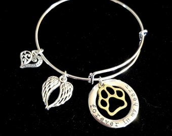 Könnte beinhalten: Silbernes Armband mit einem Herz-, Engelsflügel- und Pfotenanhänger. Der Pfotenanhänger ist mit den Worten "forever in my heart" graviert.