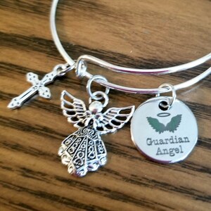 May include: Silver charm bracelet with a cross, angel, and a round charm that says "Guardian Angel" with angel wings.