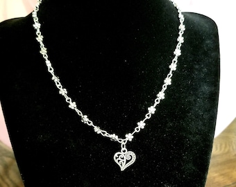 May include: A silver necklace with a delicate chain and a small, ornate heart pendant.