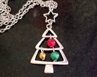 Puede incluir: Un collar de plata con un colgante de árbol de Navidad. El árbol está decorado con adornos rojos, verdes y dorados. El collar tiene un dije de estrella en la parte superior.