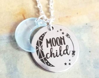 Könnte beinhalten: Eine silberne Halskette mit einem runden Anhänger, auf dem "moon child" steht, und einem Halbmond-Anhänger. Der Anhänger hat ein schwarz-weißes Design.