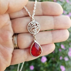 以下が含まれることがあります： 赤い涙型のペンダントとフィリグリーサークルのチャームが付いたシルバーネックレス