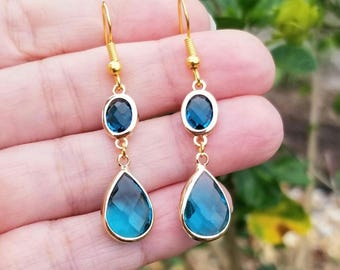 Puede incluir: Pendientes de aro de oro con dos piedras azules en forma de lágrima. La lágrima más grande está suspendida de una piedra azul más pequeña de forma ovalada.