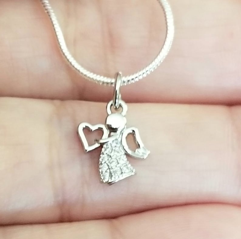 Puede incluir: Un collar de plata con un peque&ntilde;o colgante de &aacute;ngel adornado con piedras brillantes transparentes.