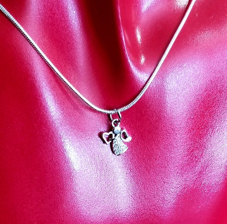 Puede incluir: Un collar de cadena de plata con un peque&ntilde;o colgante de &aacute;ngel. El &aacute;ngel tiene un halo y alas y est&aacute; adornado con peque&ntilde;os diamantes de imitaci&oacute;n transparentes.