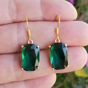 May include: A pair of gold earrings with large, emerald green, faceted, rectangular stones.
