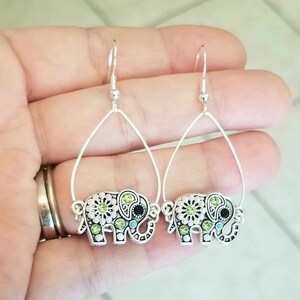 Op de afbeelding: Een paar zilveren oorhangers met een olifantendesign met groene en blauwe strass.