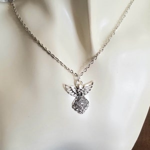 May include: A silver chain necklace with a detailed angel pendant. The angel has wings and a flowing gown.