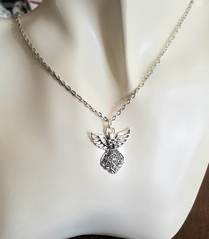 May include: A silver chain necklace with a detailed angel pendant. The angel has wings and a flowing gown.