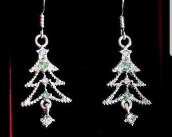 May include: A pair of silver-toned Christmas tree earrings. Each earring features a tree design with clear and green crystals. The earrings have a hook closure and a dangling square-shaped crystal at the bottom.