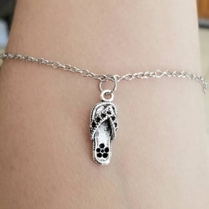 May include: A silver chain bracelet with a silver charm in the shape of a flip flop. The flip flop charm has black rhinestones.