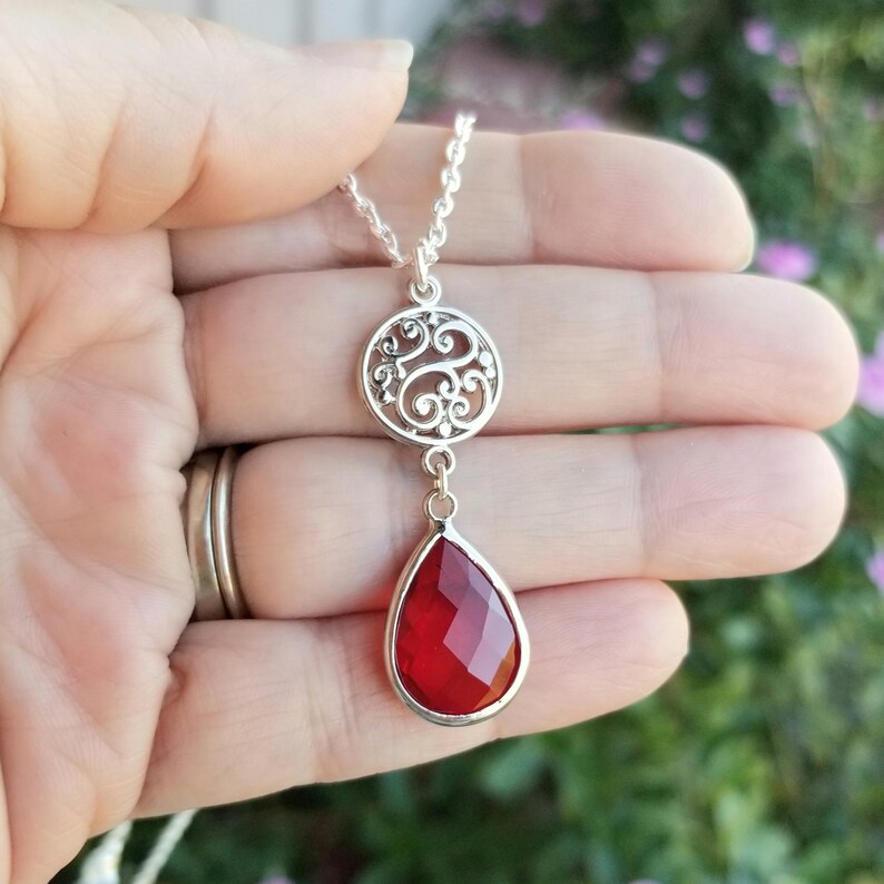 以下が含まれることがあります： フィリグリーペンダントと赤い涙型の宝石が付いたシルバーネックレス