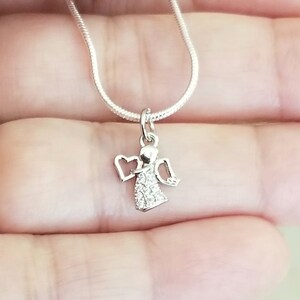 Puede incluir: Un collar de cadena de plata con un peque&ntilde;o colgante de &aacute;ngel de cristal transparente. El &aacute;ngel tiene alas y un halo en forma de coraz&oacute;n.