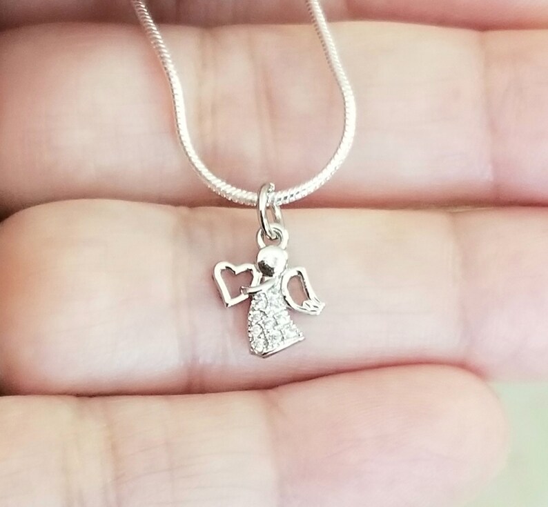 Puede incluir: Un collar de cadena de plata con un peque&ntilde;o colgante de &aacute;ngel de cristal transparente. El &aacute;ngel tiene alas y un halo en forma de coraz&oacute;n.