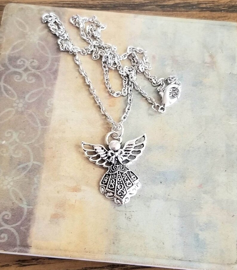 May include: A silver chain necklace with an angel pendant. The angel has detailed wings and a flowing gown.