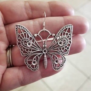 May include: Silver butterfly earrings with a delicate filigree design. The earrings have a hook closure.