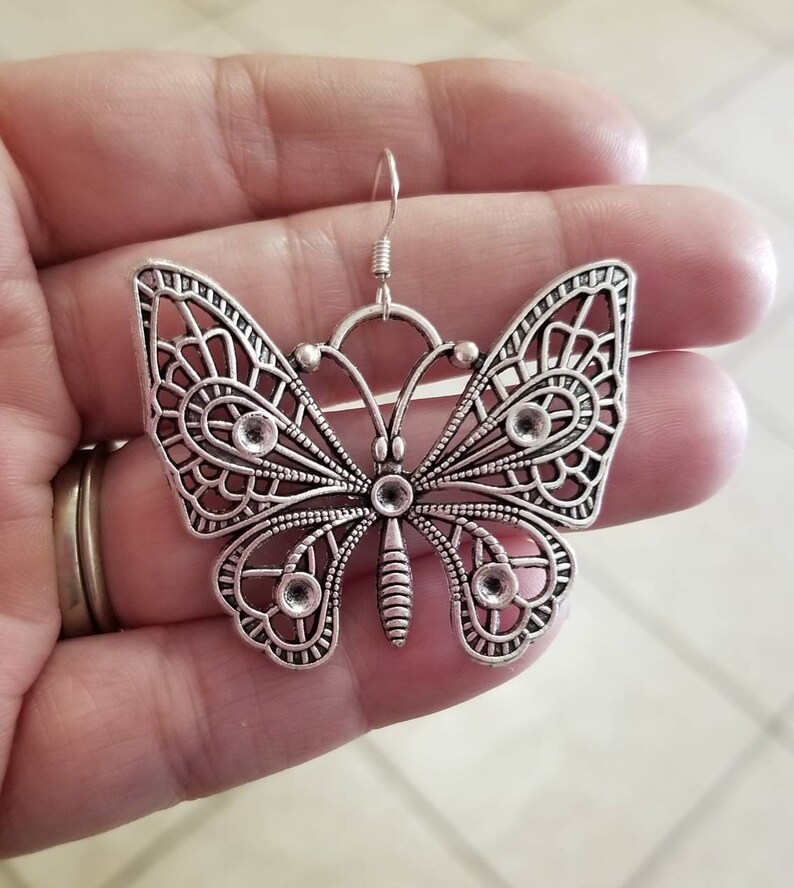 May include: Silver butterfly earrings with a delicate filigree design. The earrings have a hook closure.