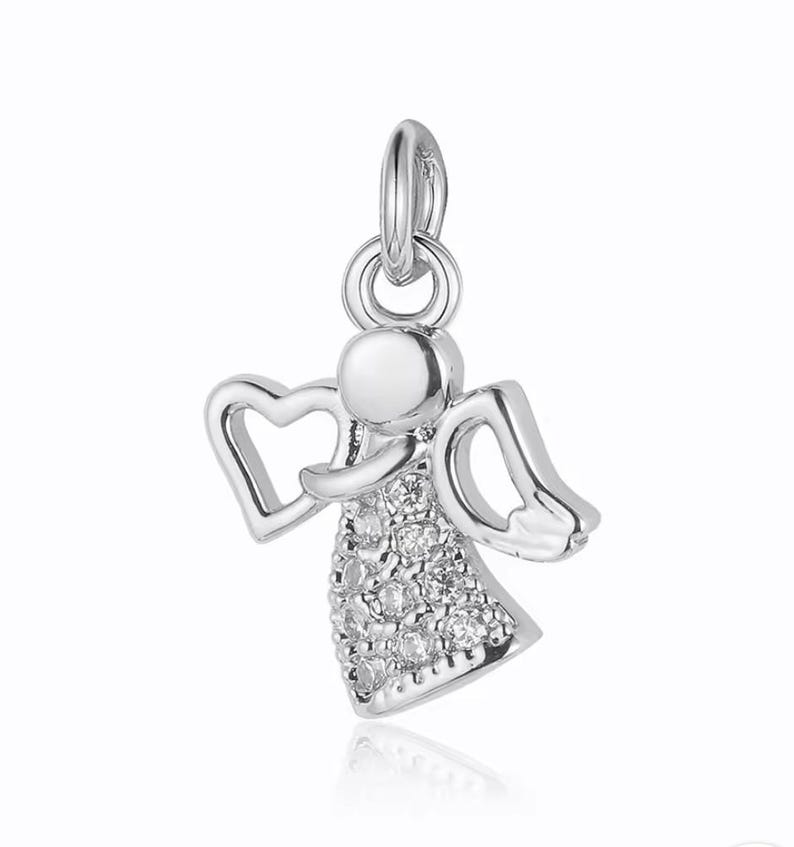 Puede incluir: Un amuleto de &aacute;ngel de plata con detalles de cristal transparente. El &aacute;ngel tiene las alas extendidas y un halo.