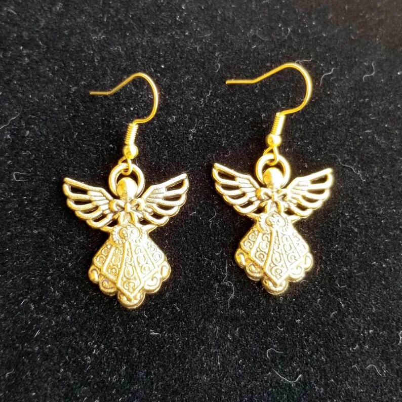Puede incluir: Un par de pendientes dorados con forma de &aacute;ngel. Cada pendiente presenta una figura de &aacute;ngel detallada con alas extendidas y un vestido fluido. Los pendientes tienen un dise&ntilde;o de gancho simple para un uso f&aacute;cil.