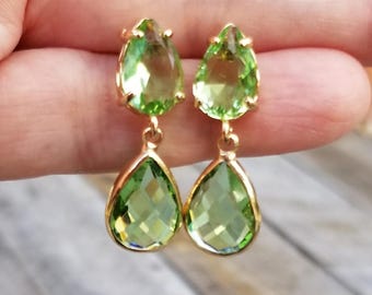May include: Gold-coloured drop earrings with pear-shaped, faceted, light green gemstones. The earrings have a simple, elegant design with a gold setting around the stones. The earrings are a light, bright green colour.