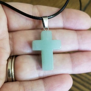 May include: A light green jade cross pendant on a black cord necklace.