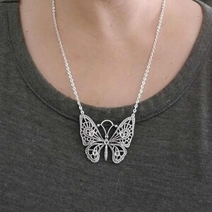 May include: A silver chain necklace with a large, detailed butterfly pendant. The butterfly has a delicate, filigree design and is adorned with small, clear crystals.