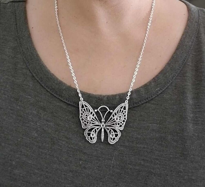 May include: A silver chain necklace with a large, detailed butterfly pendant. The butterfly has a delicate, filigree design and is adorned with small, clear crystals.