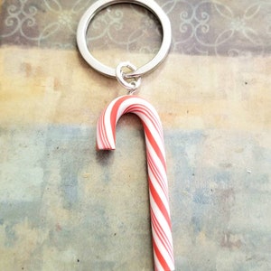 May include: A red and white candy cane keychain. The candy cane is made of polymer clay and is attached to a silver key ring.
