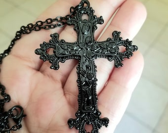 May include: Black filigree cross pendant necklace. The ornate cross features floral and scrollwork details. The necklace has a matching black chain and clasp. The gothic-style pendant is a religious accessory.