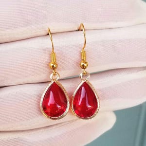 May include: A pair of gold dangle earrings with red teardrop-shaped stones.