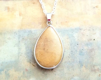 May include: A teardrop-shaped pendant necklace with a light brown stone set in a silver frame. The necklace is on a silver chain.
