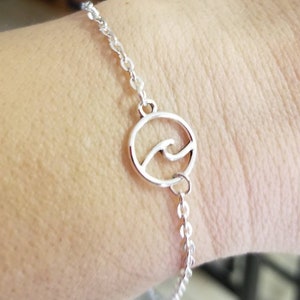 May include: A silver chain bracelet with a circular charm featuring a wave design.