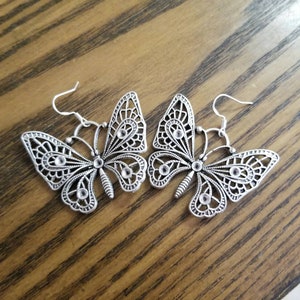 May include: A pair of silver butterfly earrings with clear rhinestone accents. The earrings have a delicate, intricate design and are perfect for adding a touch of elegance to any outfit.
