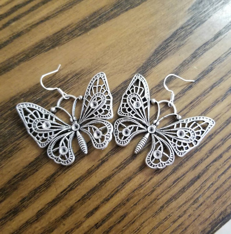 May include: A pair of silver butterfly earrings with clear rhinestone accents. The earrings have a delicate, intricate design and are perfect for adding a touch of elegance to any outfit.