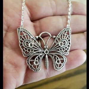 May include: A silver butterfly necklace with clear rhinestone accents. The butterfly is detailed with intricate filigree work.