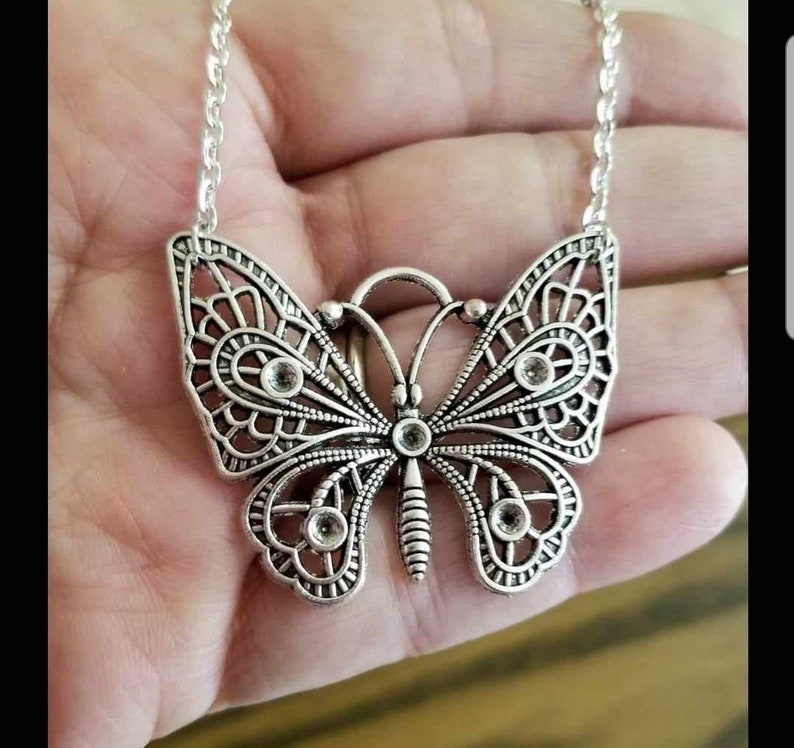 May include: A silver butterfly necklace with clear rhinestone accents. The butterfly is detailed with intricate filigree work.