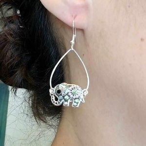 Op de afbeelding: Zilveren oorhangers met een groene en roze olifantbedel. De olifant heeft een bloemmotief en zwarte ogen.