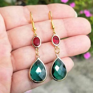 May include: Gold dangle earrings with a teardrop-shaped green gemstone and a smaller red gemstone above it.