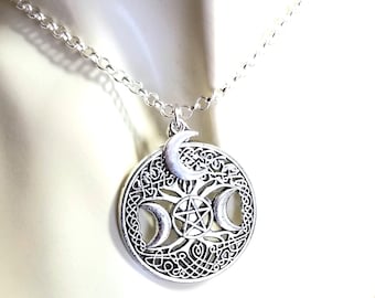 May include: A silver-toned circular pendant necklace featuring a central pentagram surrounded by three crescent moons and intricate Celtic knotwork patterns. The pendant hangs from a simple silver-toned link chain, showcasing a detailed metallic finish.