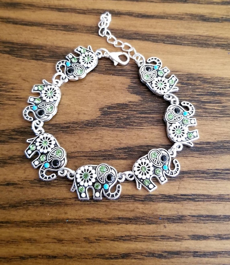 Op de afbeelding: Zilveren armband met zeven olifantenbedels. Elke olifantenbedel is versierd met groene, witte en blauwe strasssteentjes.