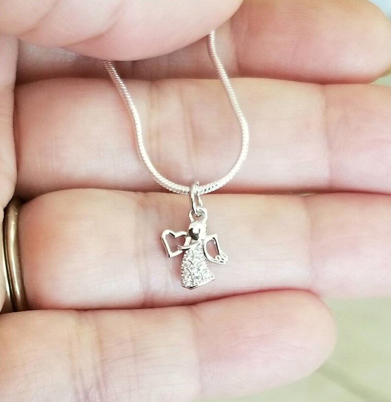 Puede incluir: Un collar de cadena de plata con un peque&ntilde;o colgante de &aacute;ngel de cristal transparente.