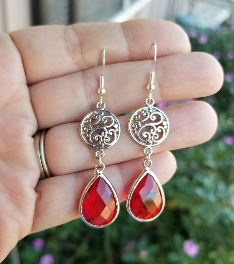 以下が含まれることがあります： 赤い涙型のクリスタルとフィリグリーのデザインが施されたシルバーのドロップイヤリング