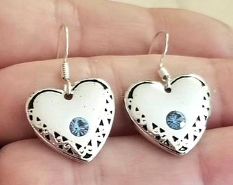 May include: A pair of silver-toned heart-shaped drop earrings featuring a delicate filigree pattern along the edges and a single small, round, light blue crystal set in the center of each heart, suspended from simple silver-toned earring hooks.