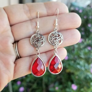 以下が含まれることがあります： 赤い涙型の宝石が付いたシルバーのドロップイヤリング。イヤリングはフィリグリーのデザインです。